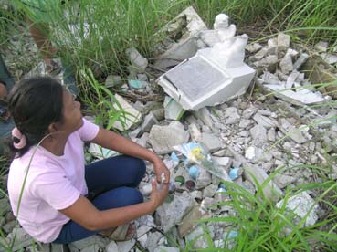 破壊された息子の墓に供え物を置くマリベスさん=首都圏マニラ市の北部墓地で1日写す