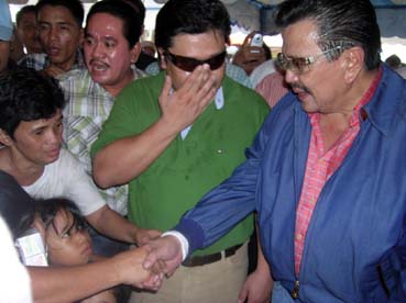 集まった支持者と握手するエストラダ前大統領(右)=マニラ市トンドで午前11時45分ごろ写す