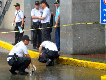 手投げ弾とみられる爆発物がさく裂した現場を調べる捜査員ら。付近の柱や壁には飛散した破片の痕跡も=29日午前11時半ごろ、オルティガス通りで写す