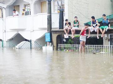 1階部分がほぼ水没し、屋根に上って救出を待つ住民ら=7日午前10時半ごろ、首都圏ケソン市ノバリチェスで写す