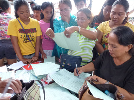 仮の役場スペースで住民分の社会福祉開発省の世帯登録カードにサインをする議長のモンタルバンさん(右端)=12月21日、ビサヤ地方レイテ州タクロバン市バランガイ88で写す