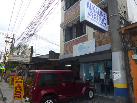 販売店の前に掲げられた「アルカリン」飲料水の看板=1月29日午後5時ごろ、首都圏マカティ市で写す