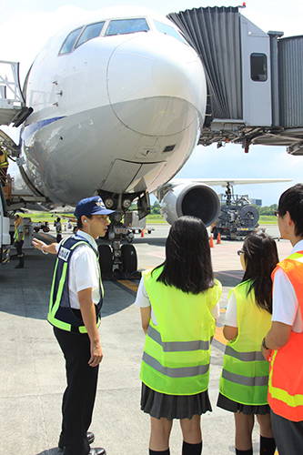 マニラ空港駐機場で仕事の説明を聞く高校生ら=11日午後1時40分ごろ、マニラ空港駐機場で写す