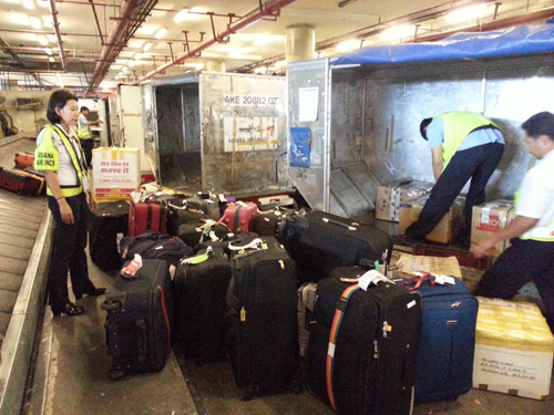 コンテナに預け入れ手荷物を積み込む地上職員=23日午前、首都圏パサイ市のマニラ空港第1ターミナルで写す