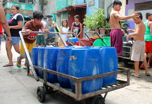 くみ置きの水を入れた、タンクを運ぶトンド地区の住民=11日午後2時15分ごろ首都圏マニラ市トンド地区で写す