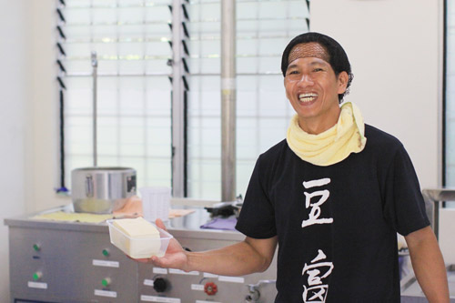 出来たての豆腐を手に笑顔を見せるパアスさん=リサール州モンタルバン町で写す