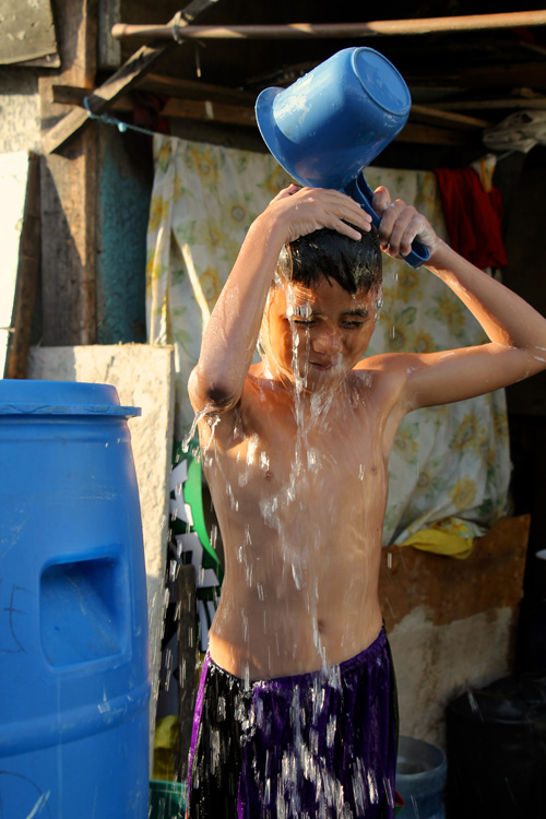 猛暑の中、夕日を浴びながら道端で水浴びをするクリストファー・レイエスくん=31日午後4時半すぎ、首都圏マカティ市で冨田すみれ子写す