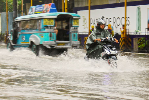 冠水した道路を水しぶきを上げながら走るオートバイ=13日午後5時ごろ、首都圏マカティ市で冨田すみれ子写す