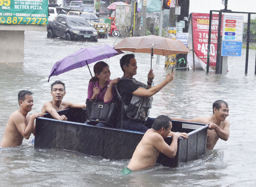 浸水した道路で通行者を運ぶ住民ら=12日午後3時ごろ、首都圏ケソン市バナウエ地区で伊藤明日香撮影