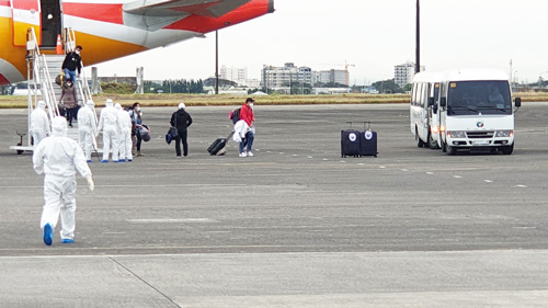 9日に中国・武漢からクラーク国際空港に到着した政府チャーター便から降りる比人たちと誘導する防護服姿の政府職員ら(AFP=時事)