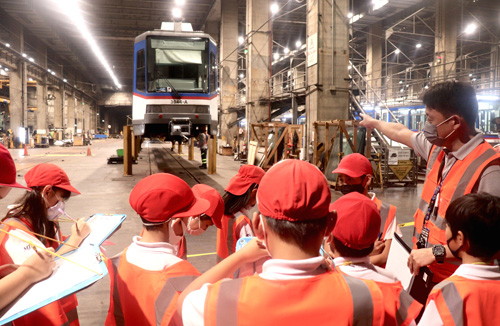 マニラ日本人学校の4年生児童にMRT3の車庫内を案内するTESフィリピンの車両部シニアマネジャー岩津雅さん(右端)=6日午前、首都圏ケソン市で岡田薫撮影