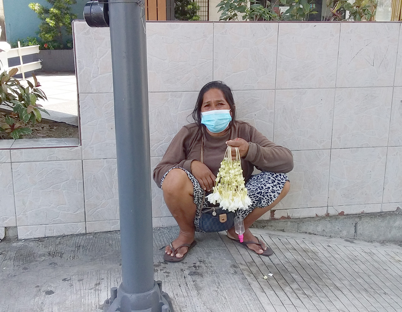 路上で花(サンパギータ)を20ペソで売る女性。記者に生活の苦しさを訴えていた=21年、首都圏マカティ市で竹下友章撮影