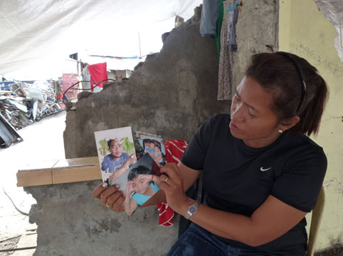 高潮で大破した自宅で、亡くなった夫と3人の子供の写真を手に取るマリリンさん=12月21日、ビサヤ地方レイテ州パロ町コゴンで写す