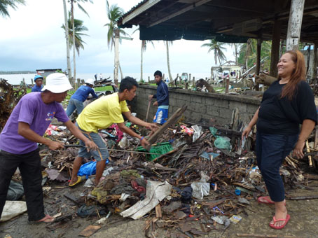 がれき撤去に雇用された住民らと話す議長のタブンガルさん(右端)。20メートルほど先には海が広がる=12月22日、ビサヤ地方サマール州バセイ町ロヨで写す